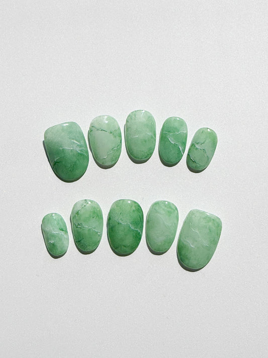Set of green marbled press-on nails on a light gray background
