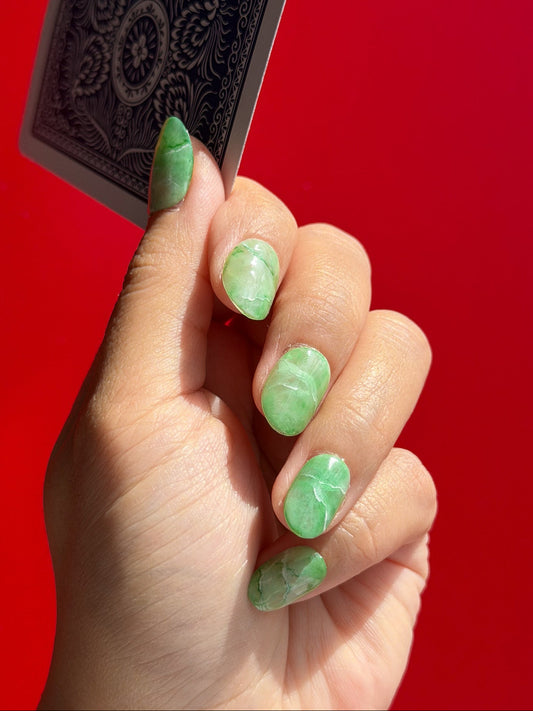 Hand with green nail polish holding a black playing card against a red background